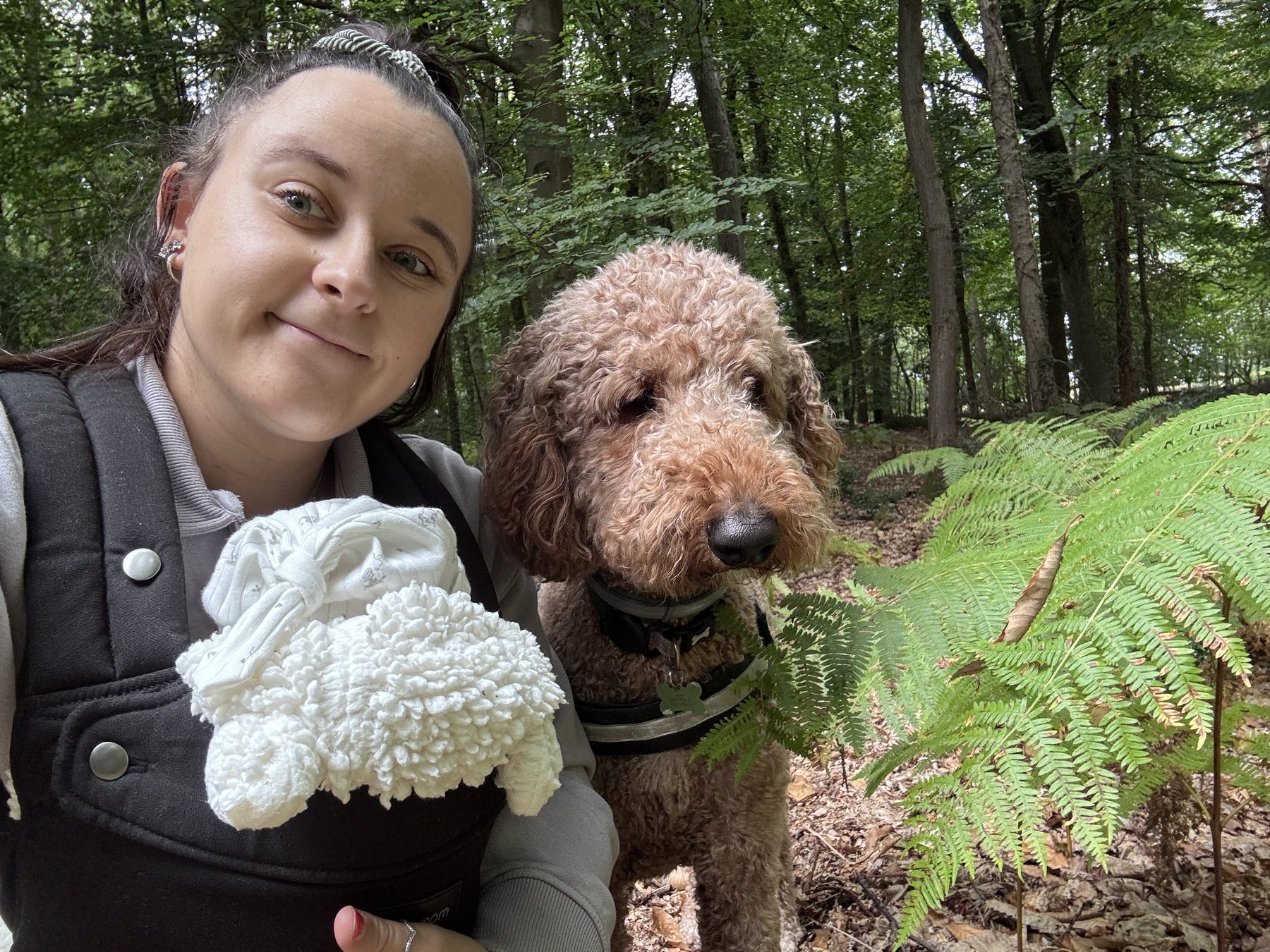 Alethea in the woods with the baby in a carrier and the dog